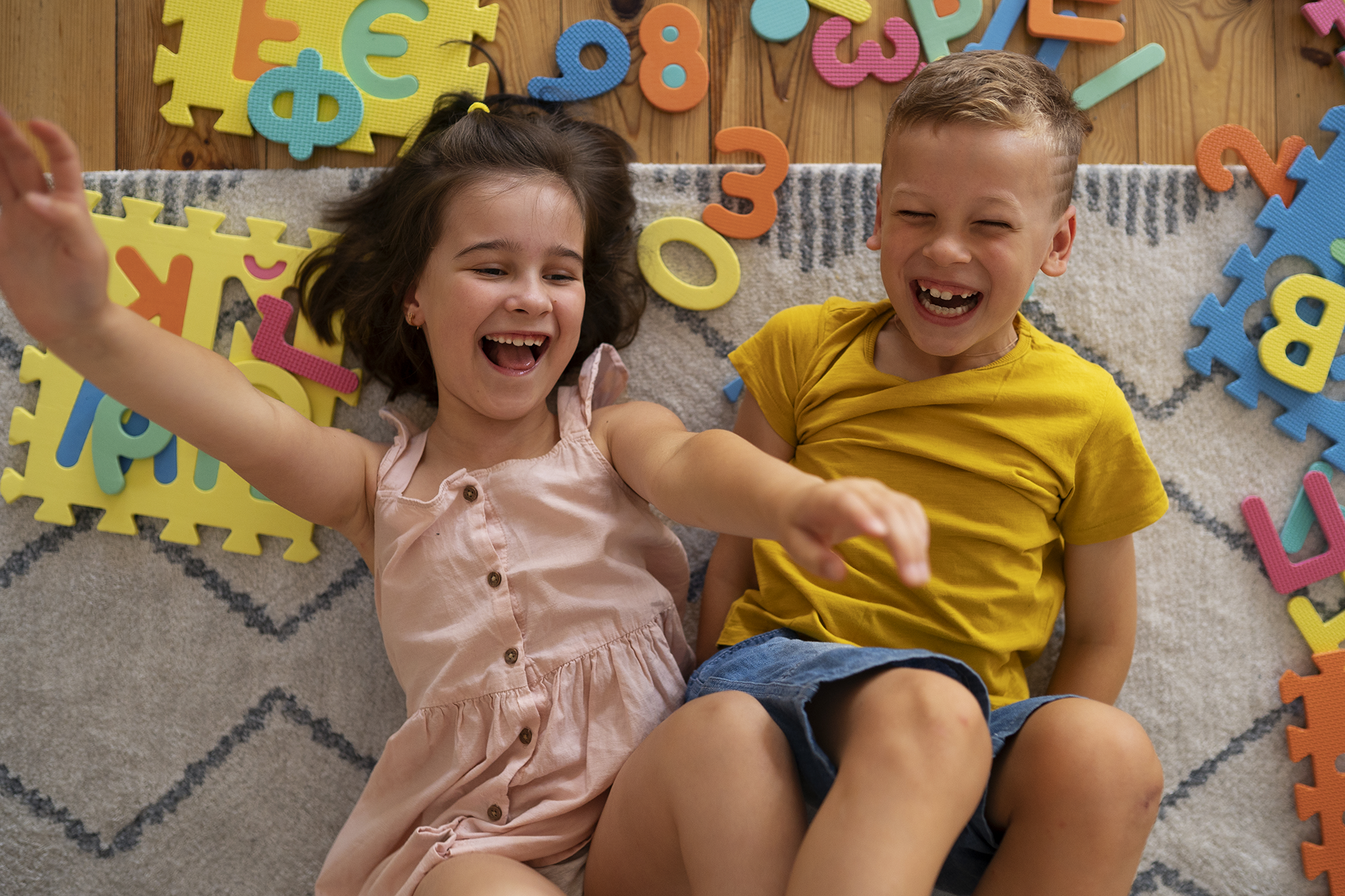 Niña y niño sonriendo sobre una alfombra jugando con letras y números de espuma durante una sesión de neurodesarrollo en NeuroKite Quito.